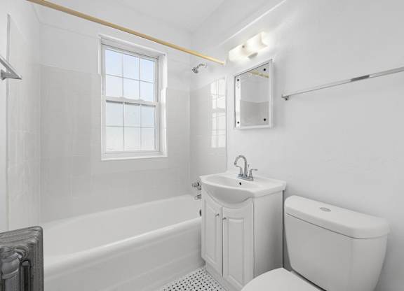 A white bathroom with a tub, toilet, sink, and mirror at Pleasant Oak Apartments, Oak Park, IL, 60302