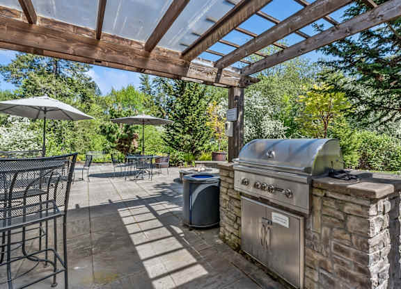 A BBQ grill is on a patio with a table and chairs.