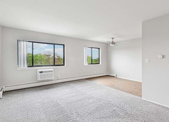 A spacious room with a grey carpet and kitchen in the background