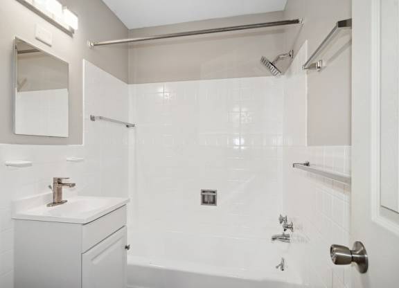 A white bathroom with a sink, mirror, and shower.
