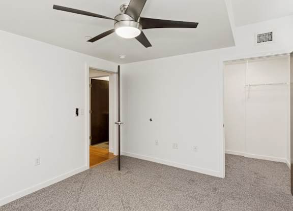 A room with a ceiling fan and a door leading to another room.