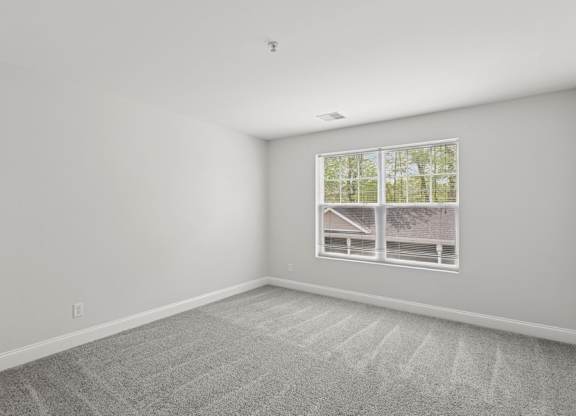 A room with a carpeted floor and a window showing a house and trees outside.