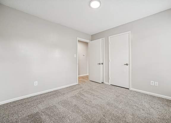 A room with a carpeted floor and three doors.