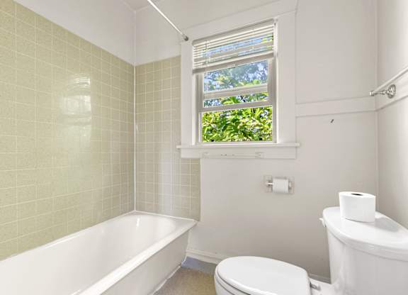 A white toilet sits next to a bathtub in a bathroom with a window.