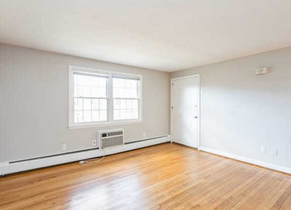 an empty room with wood floors, a white wall, and window