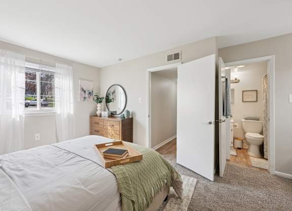 A bedroom with a bed, nightstand, and a bathroom visible through the open door.