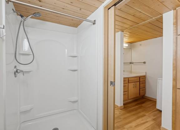 A white bathroom with wooden ceiling and floor.
