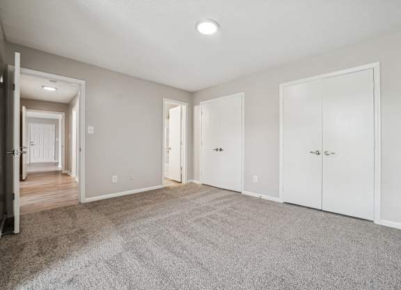 A spacious room with white doors and carpeted floor.