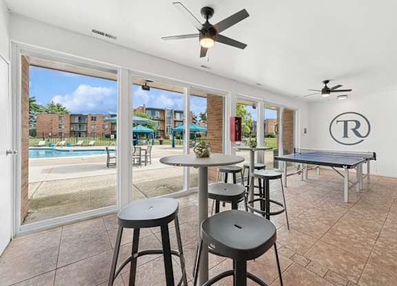 A room with a pool outside the window and a table with stools.