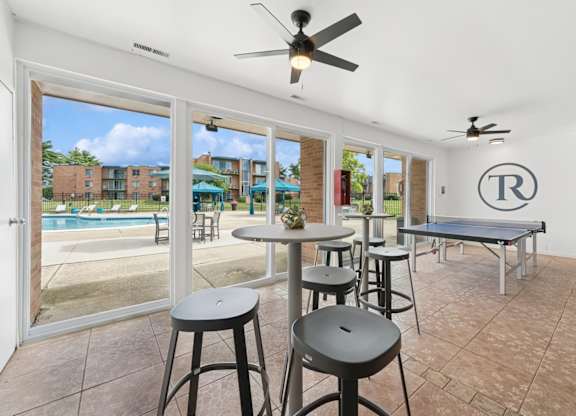 A room with a pool outside the window and a table with chairs.