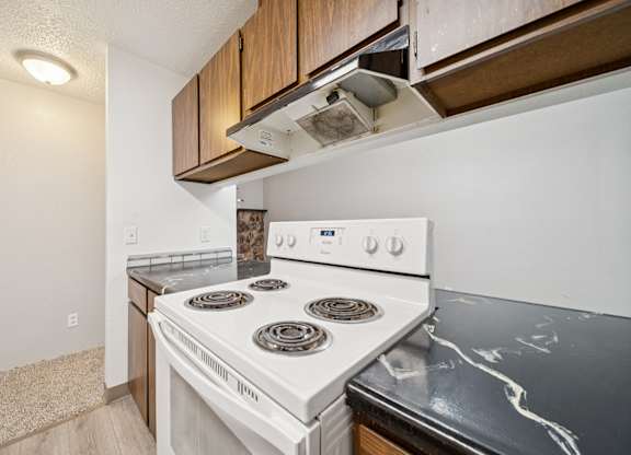 A white stove top oven with four burners is in a kitchen with a black counter top.