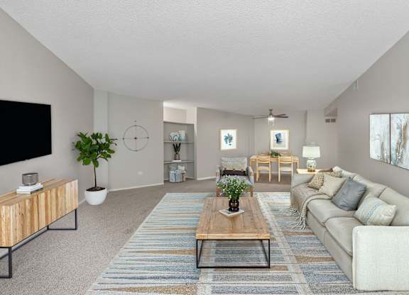 A living room with a white couch, a wooden coffee table, and a flat-screen TV mounted on the wall.