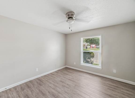 A room with a ceiling fan and a window showing a view of a house and trees.