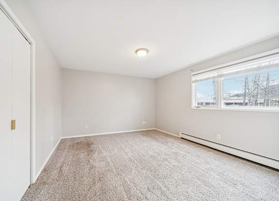 A room with a carpeted floor and a window showing a view of buildings outside.
