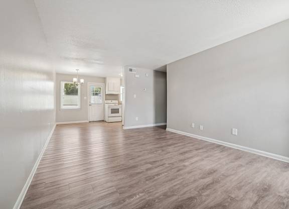 A spacious room with wood flooring and a kitchen in the background.