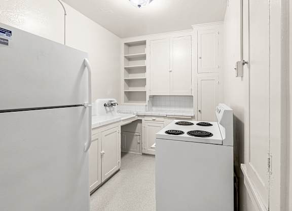 A white kitchen with a refrigerator, stove, and cabinets.