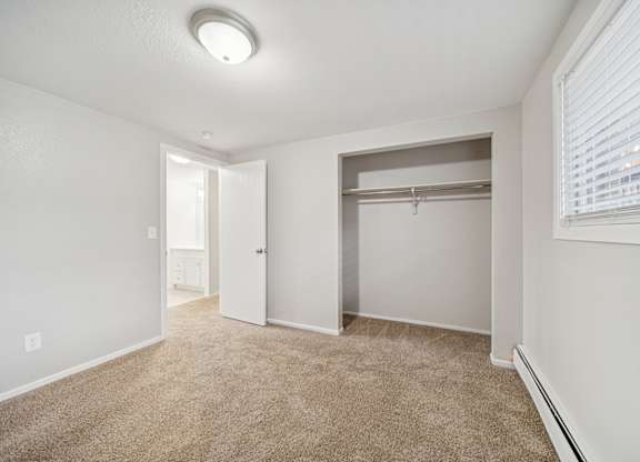 A room with a carpeted floor and a closet with a shelf.