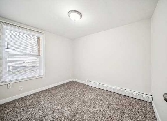 A room with a carpeted floor and a window with blinds.