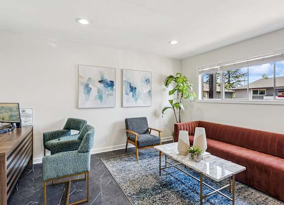 A waiting room with a red couch, a green chair, and a wooden desk.