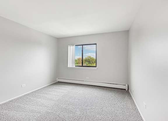 A bedroom with a window and a carpeted floor.
