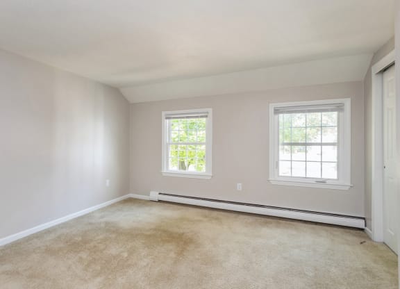 an empty bedroom with two windows and a carpeted floor