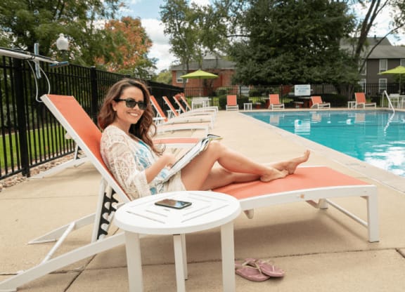 a woman sits in a chair next to a pool with a laptop on her lap at The View Apartments St Charles, St Charles, 60174