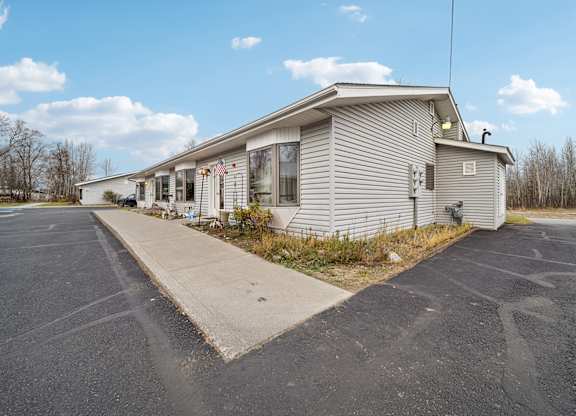 A house with a grey siding and a white roof is surrounded by a parking lot.