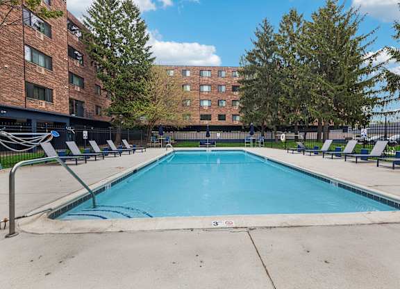A swimming pool in front of a brick building with trees around.