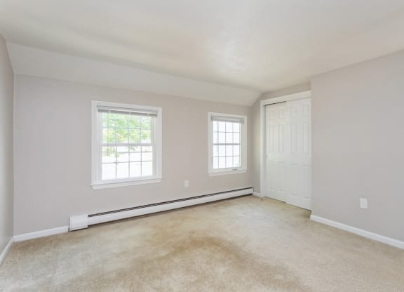 Empty carpeted room with closet door and two windows