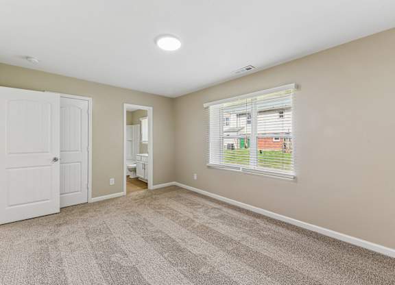 A room with a carpeted floor and a window with blinds.
