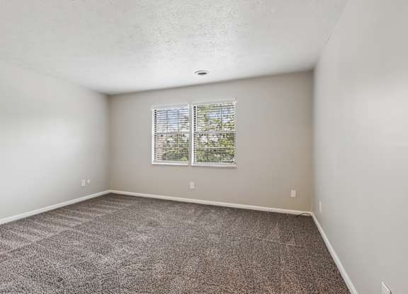 A room with a carpeted floor and a window with blinds.