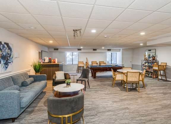 Community room with a grey sofa, a coffee table, and a dining table set up with chairs.