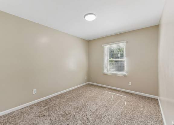 A room with a carpeted floor and a window with blinds.