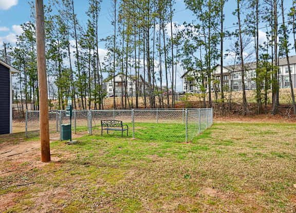 A grassy field with a fence and a bench in the foreground and a house in the background.