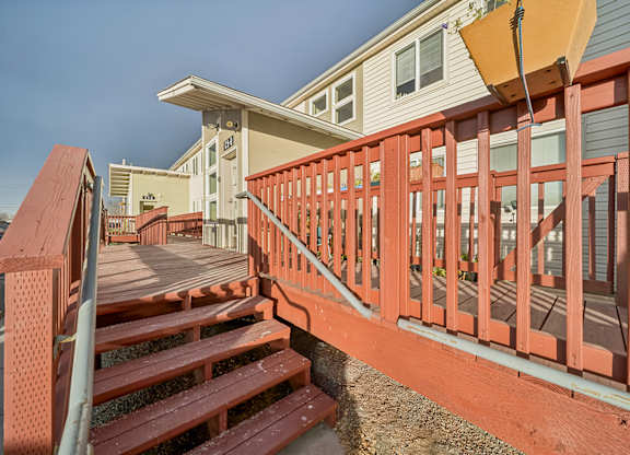 A wooden deck with a red railing and steps leading to a house.