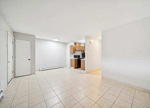 A room with white walls and a tiled floor with a door on the left and a desk with a chair in the middle.