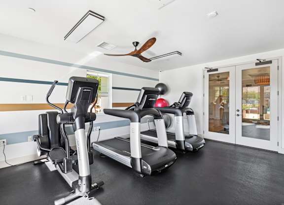 A gym with a treadmill, elliptical trainer and a fan.