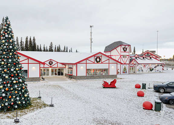 A large Christmas tree stands in front of a red building.