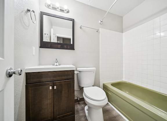 A white toilet sits next to a green bathtub in a bathroom.