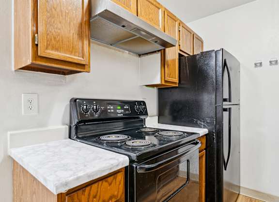 A black stove and refrigerator in a kitchen with wooden cabinets.