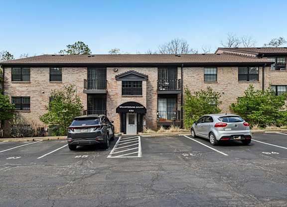 A parking lot in front of a brick building with two cars parked.