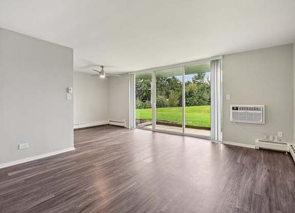 A room with wooden floors and sliding glass doors leading to a green outdoor area.