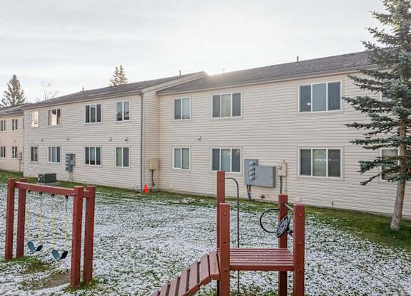A playground with a swing set and a basketball hoop in front of apartment buildings.