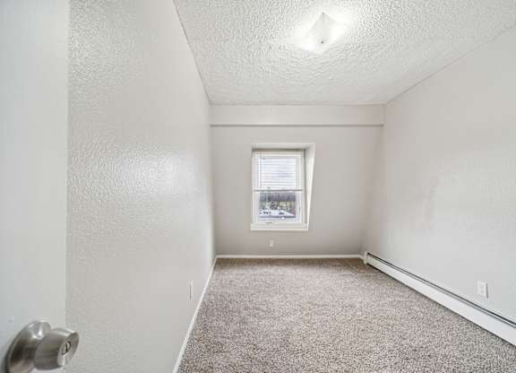 A small, empty room with a carpeted floor and a window.