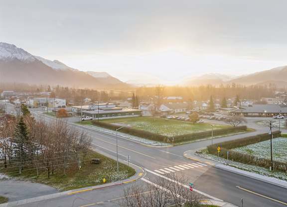 A street view of a residential area with houses, trees, and mountains in the background.