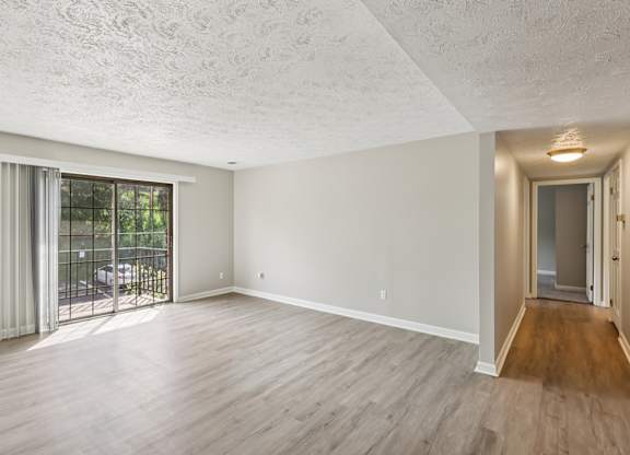 A spacious room with wooden flooring and a sliding glass door leading to a patio.