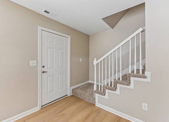 A white door is on the left and a staircase with a beige carpet is on the right.