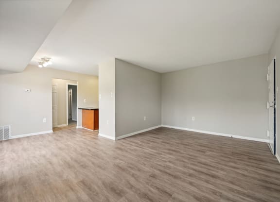 an empty living room with wood flooring and a view to a kitchen at ReNew Odenton