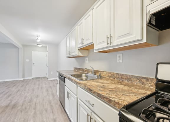 an empty kitchen with white cabinets and granite counter tops and a stove and microwave at ReNew Odenton