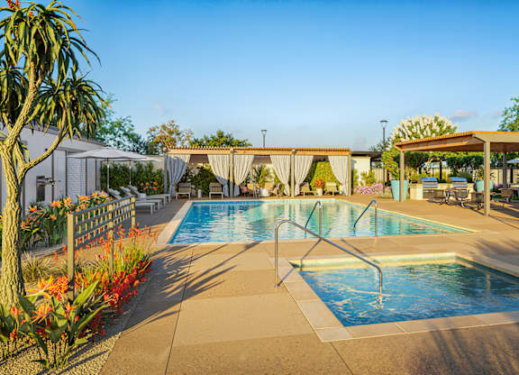 A pool surrounded by a concrete patio and a white fence.